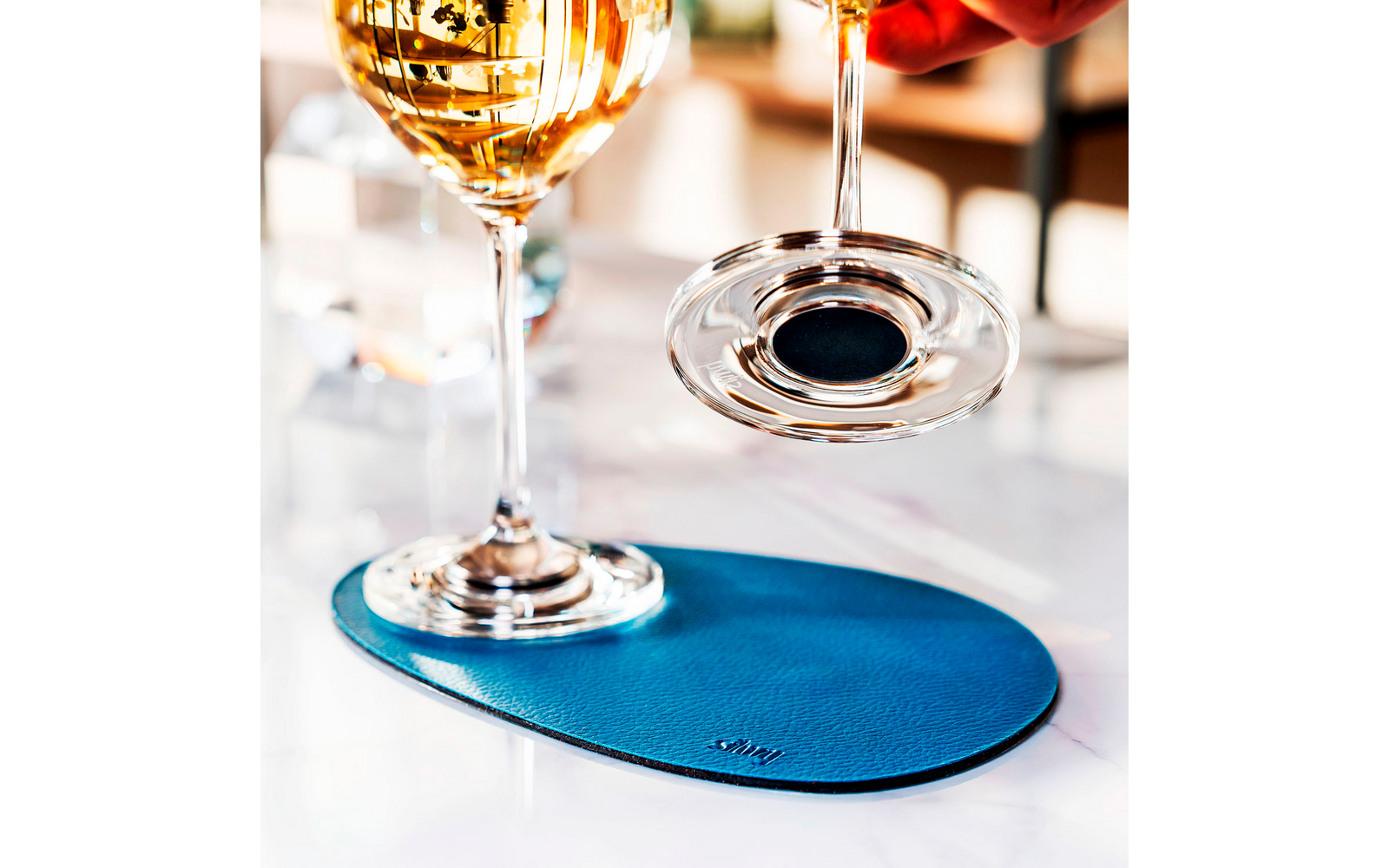 Wine glass on blue coaster with wine bottle and wine glass in the background