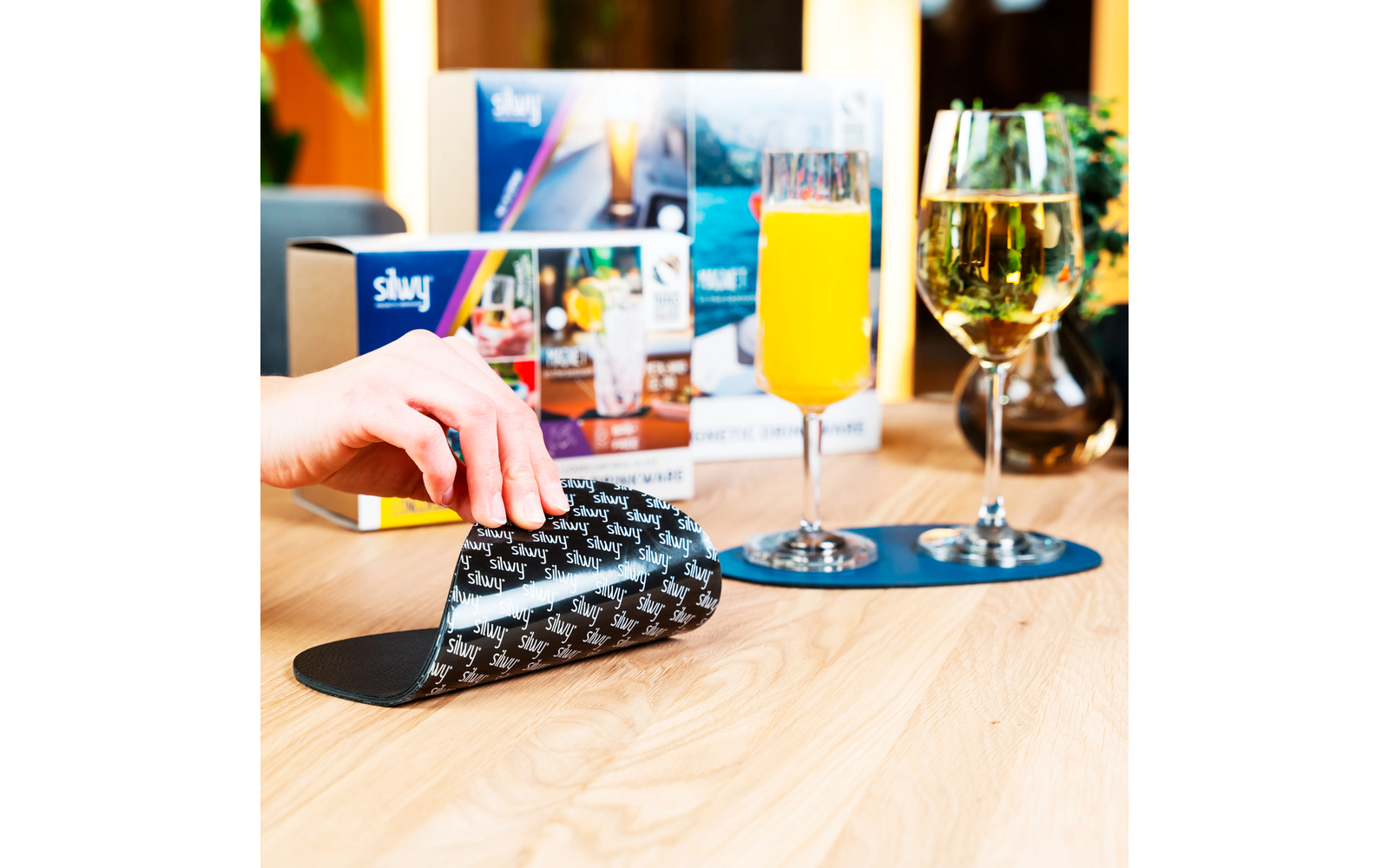 A hand pressing a bell on a wooden table with drinks and a menu