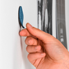 Hand hält einen blauen Klebepunkt an eine weiße Wand