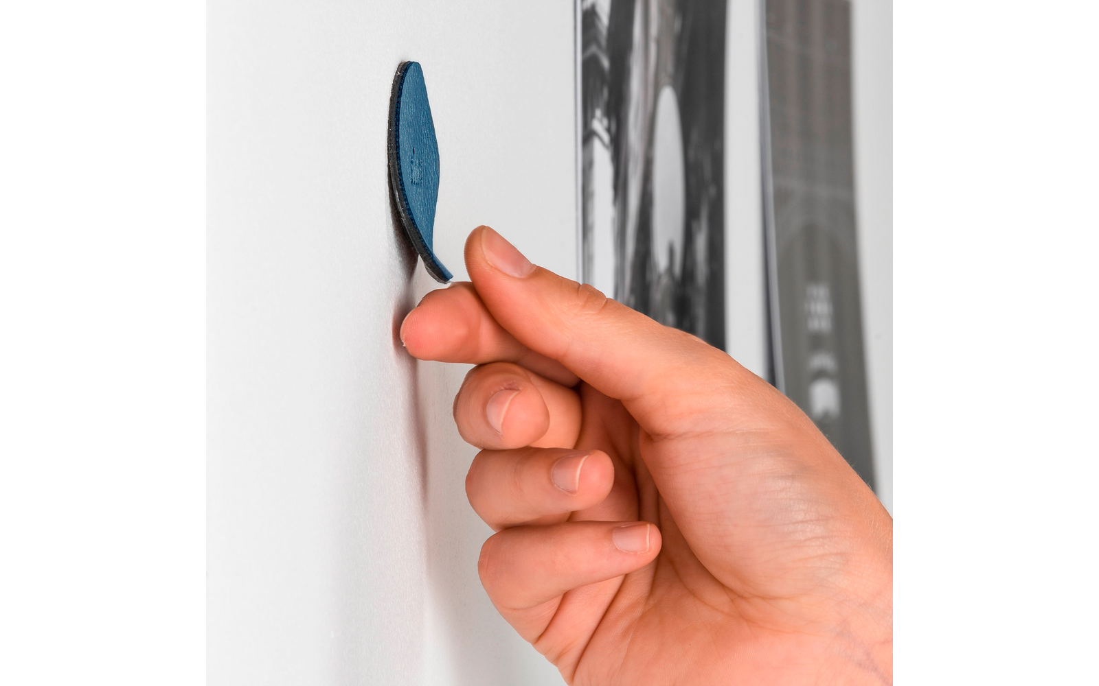 Hand hält einen blauen Klebepunkt an eine weiße Wand