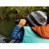 Niño con gorro y prismáticos mirando un lago con árboles al fondo
