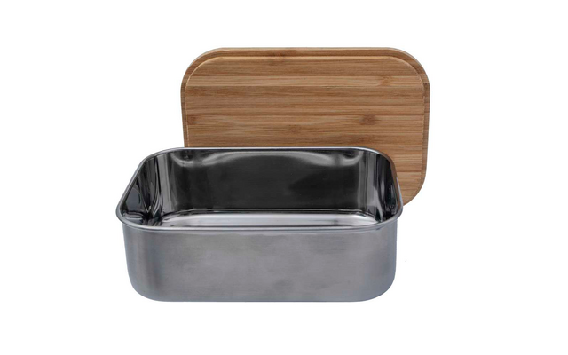 Een open rechthoekige metalen lunchtrommel met een houten deksel op de achtergrond