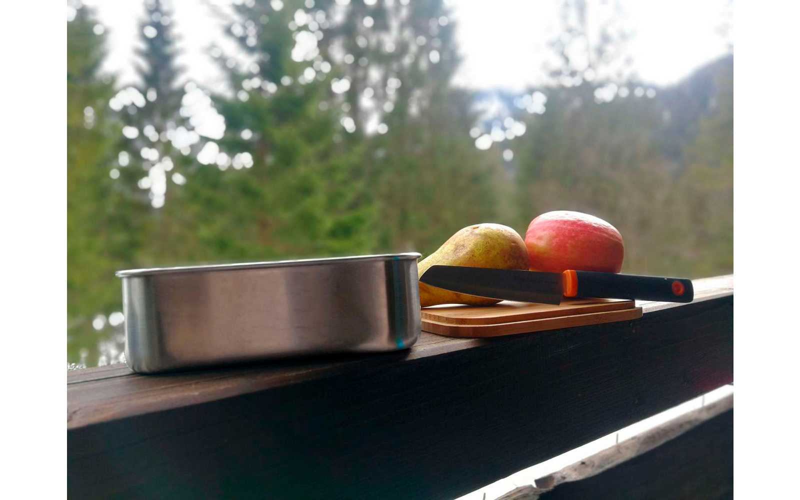 Blikken en fruit op een balkonleuning met bos en bergen op de achtergrond