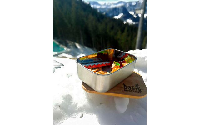 Kom met muesli en fruit, op de achtergrond besneeuwde bergen en dennenbos