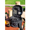 Mochila negra abierta con múltiples compartimentos, colocada sobre una mesa de madera al aire libre con césped de fondo