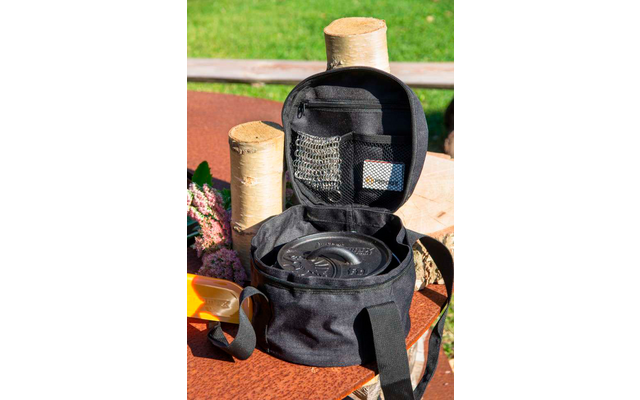 Mochila negra abierta con múltiples compartimentos, colocada sobre una mesa de madera al aire libre con césped de fondo