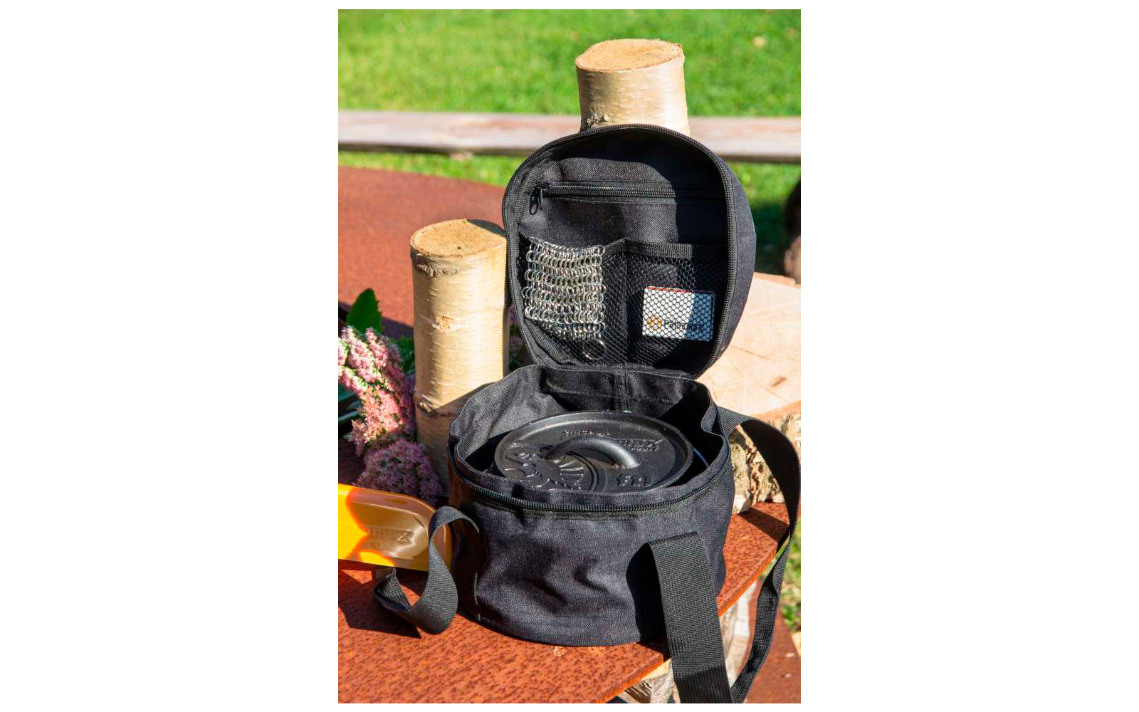 Mochila negra abierta con múltiples compartimentos, colocada sobre una mesa de madera al aire libre con césped de fondo