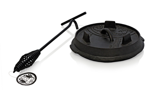 Een zwarte gietijzeren grillpan met deksel en een grilllifters met een lange steel
