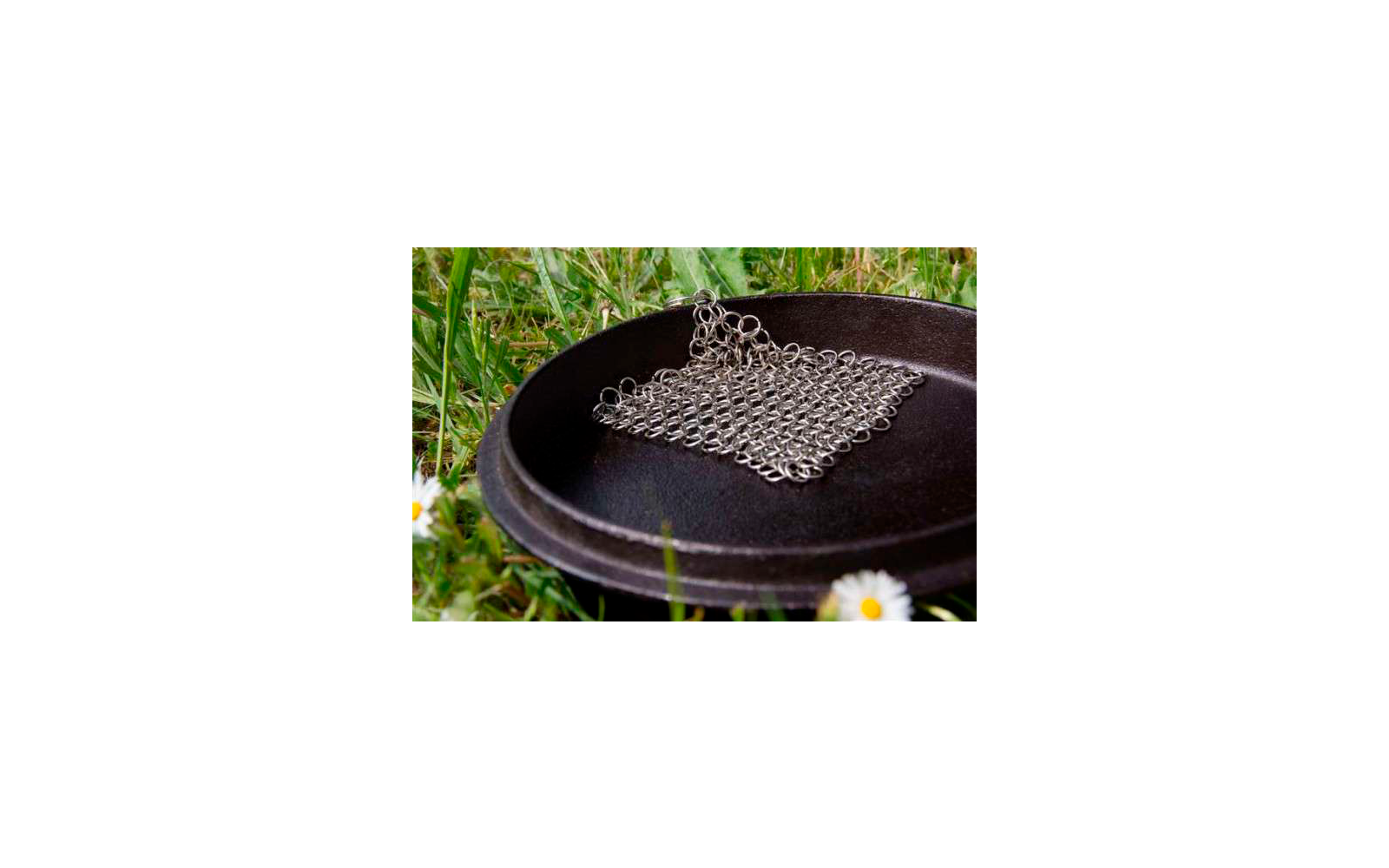 Ein quadratisches Kettenhemd aus Metall liegt auf einer schwarzen Schale im Gras
