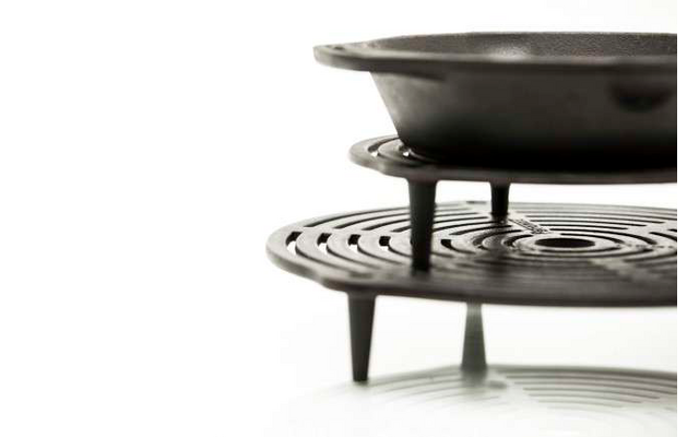 Schwarze Pfanne auf einem schwarzen Grillrost mit drei Beinen vor weißem Hintergrund