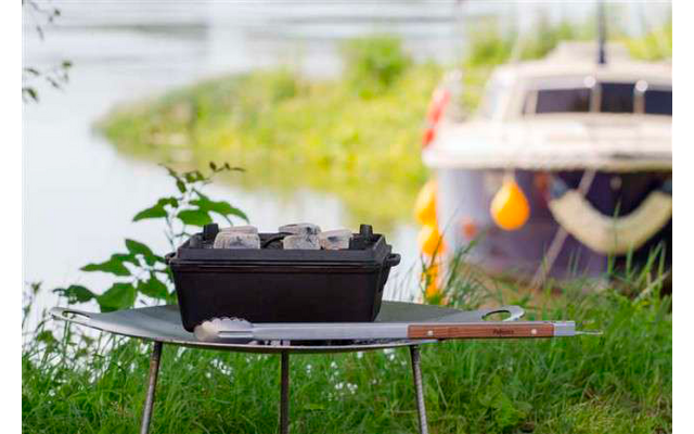 Parrilla sobre una mesa en el jardín, con un barco y plantas verdes al fondo