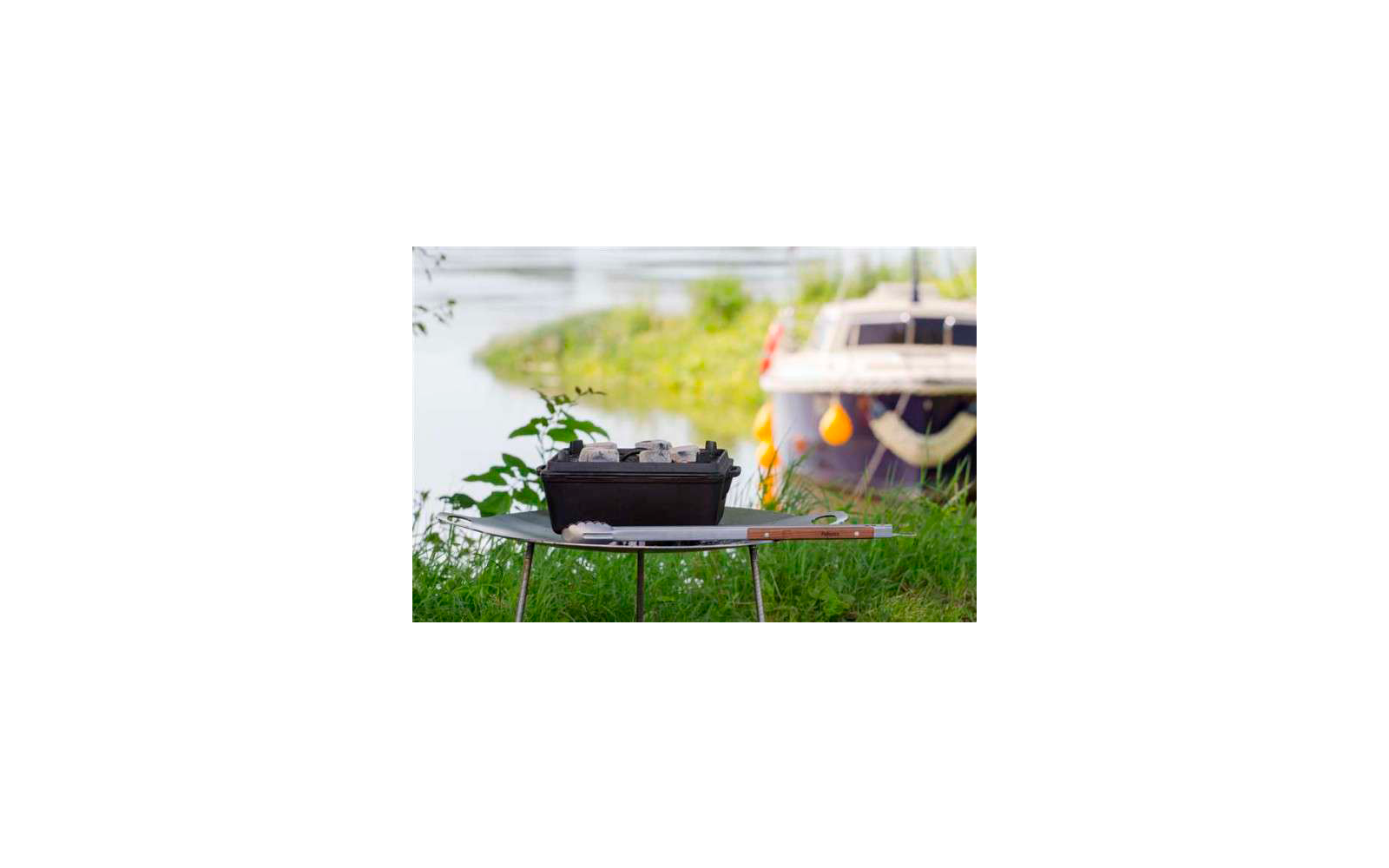 Parrilla sobre una mesa en el jardín, con un barco y plantas verdes al fondo