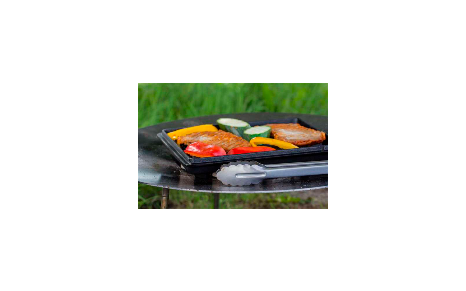 Una parrilla con varias verduras y un trozo de carne, césped de fondo