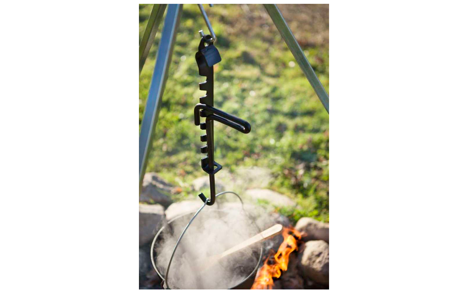 Ein schwarzer Angelrutenhalter mit Haken hängt über einem Lagerfeuer im Freien