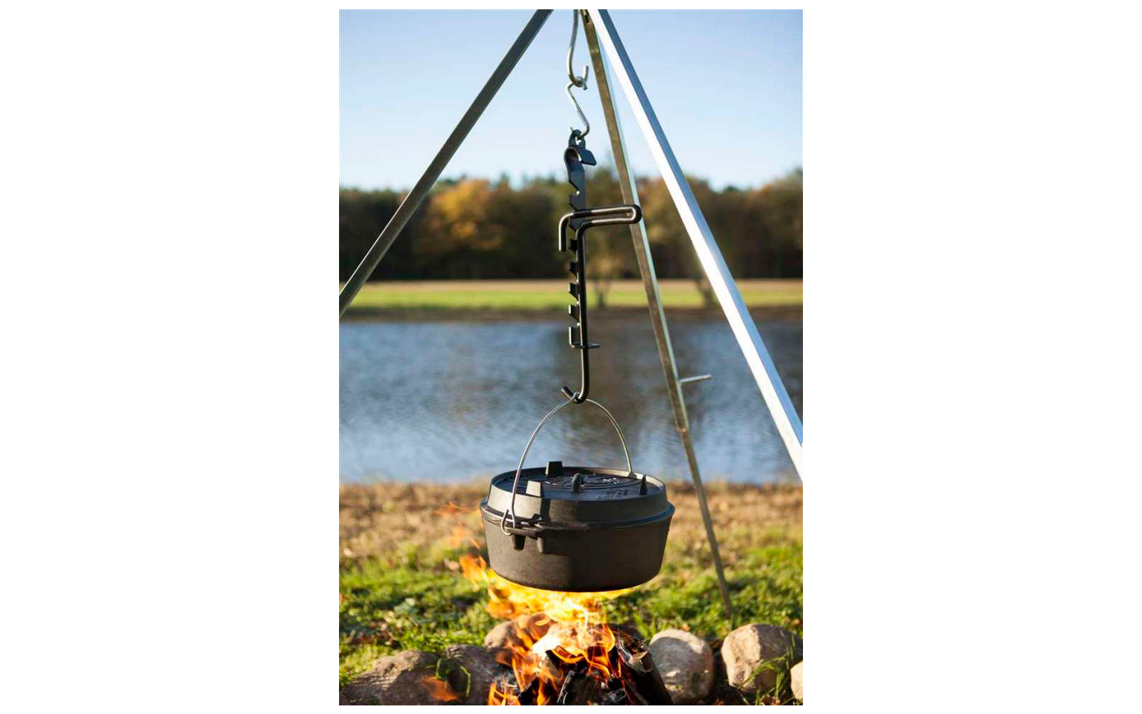 Ein schwarzer Kochtopf hängt an einem Metallgestell über einem Lagerfeuer am See
