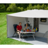 Drei Personen sitzen an einem Tisch unter einem Sonnenschirm vor einem Wohnmobil