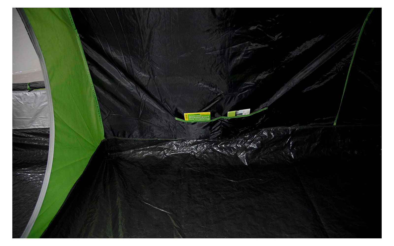 Binnenaanzicht van een tent met zwarte vloer en groene naden