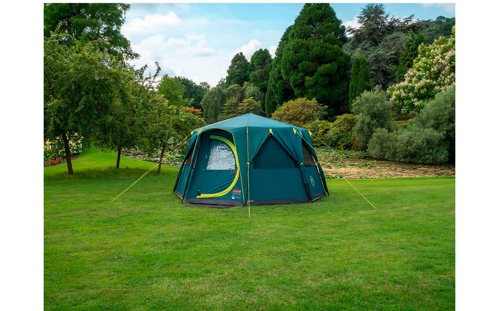 Tenda blu su un prato verde con alberi sullo sfondo