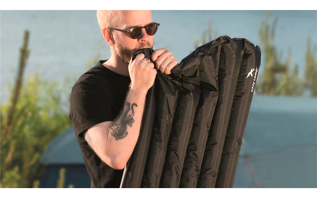 Un hombre con gafas de sol está inflando un colchón inflable negro