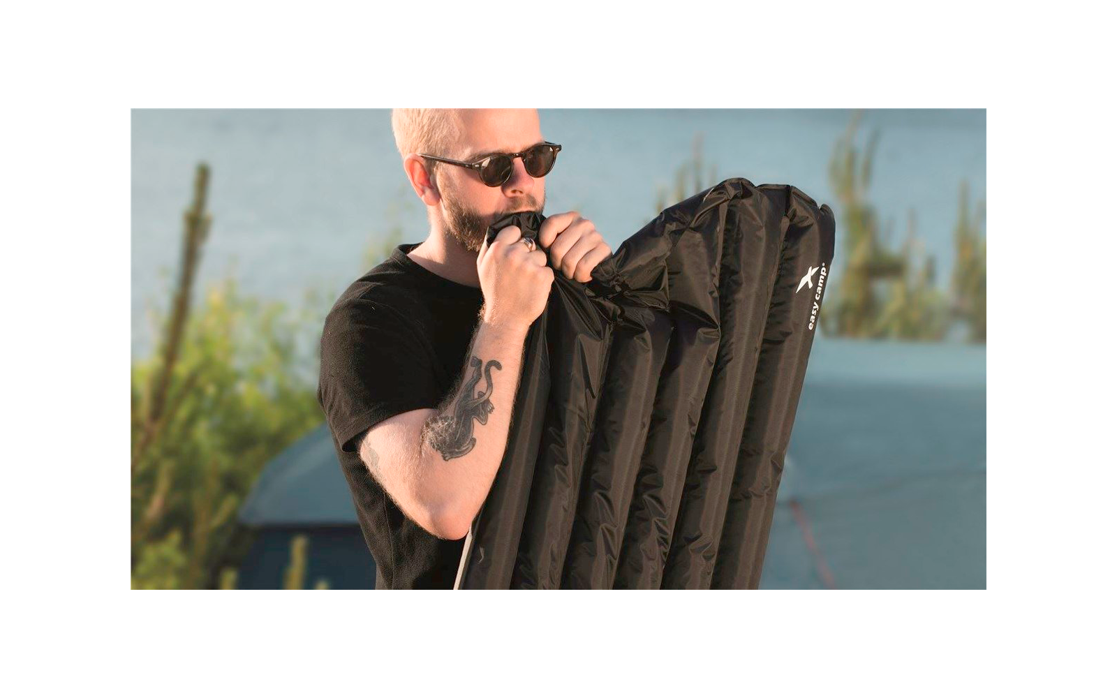Un hombre con gafas de sol está inflando un colchón inflable negro