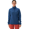 Femme portant une veste bleue et un pantalon rouge, debout devant un fond blanc