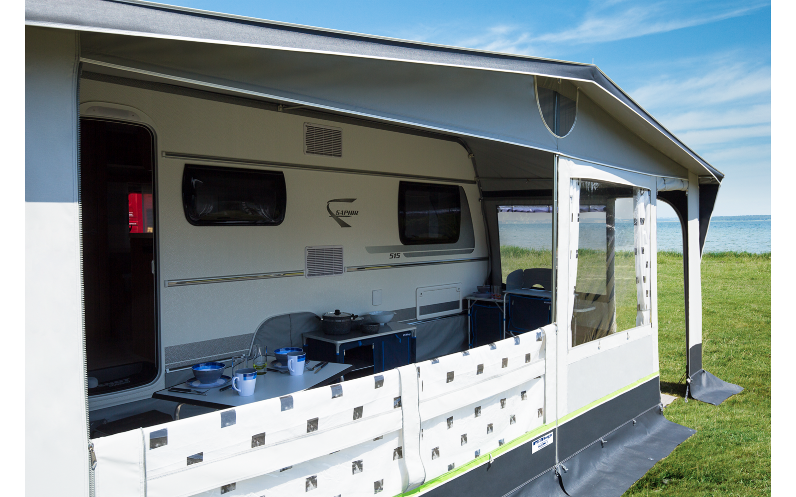 Weißer Wohnwagen mit überdachtem Sitzbereich und Tisch im Freien bei sonnigem Himmel