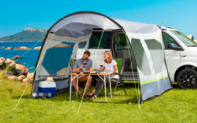 Zwei Personen sitzen an einem Campingtisch vor einem Wohnmobil mit Sicht auf das Meer