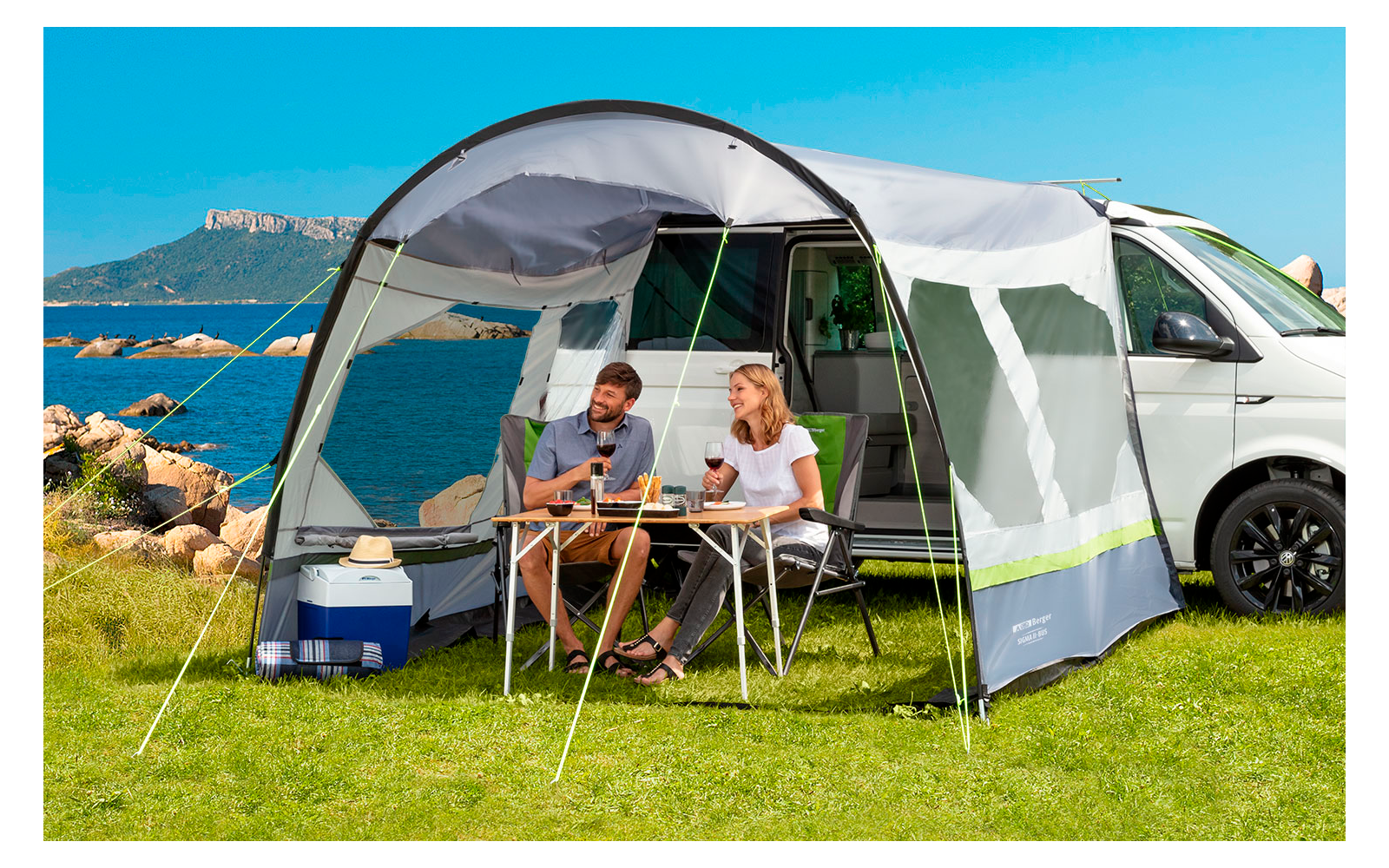 Zwei Personen sitzen an einem Campingtisch vor einem Wohnmobil mit Sicht auf das Meer