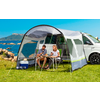 Zwei Personen sitzen an einem Campingtisch vor einem Wohnmobil mit Sicht auf das Meer