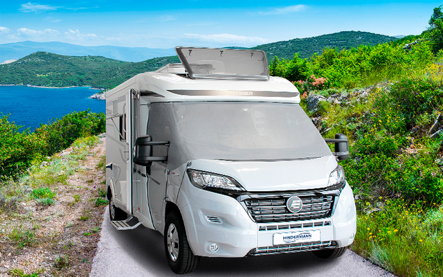 Camping-car sur une route de montagne étroite avec un lac et des collines vertes en arrière-plan