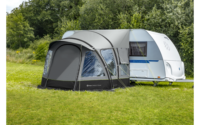 Großes graues Campingzelt mit gebogenen weißen Stangen, auf einer Wiese mit Bäumen im Hintergrund