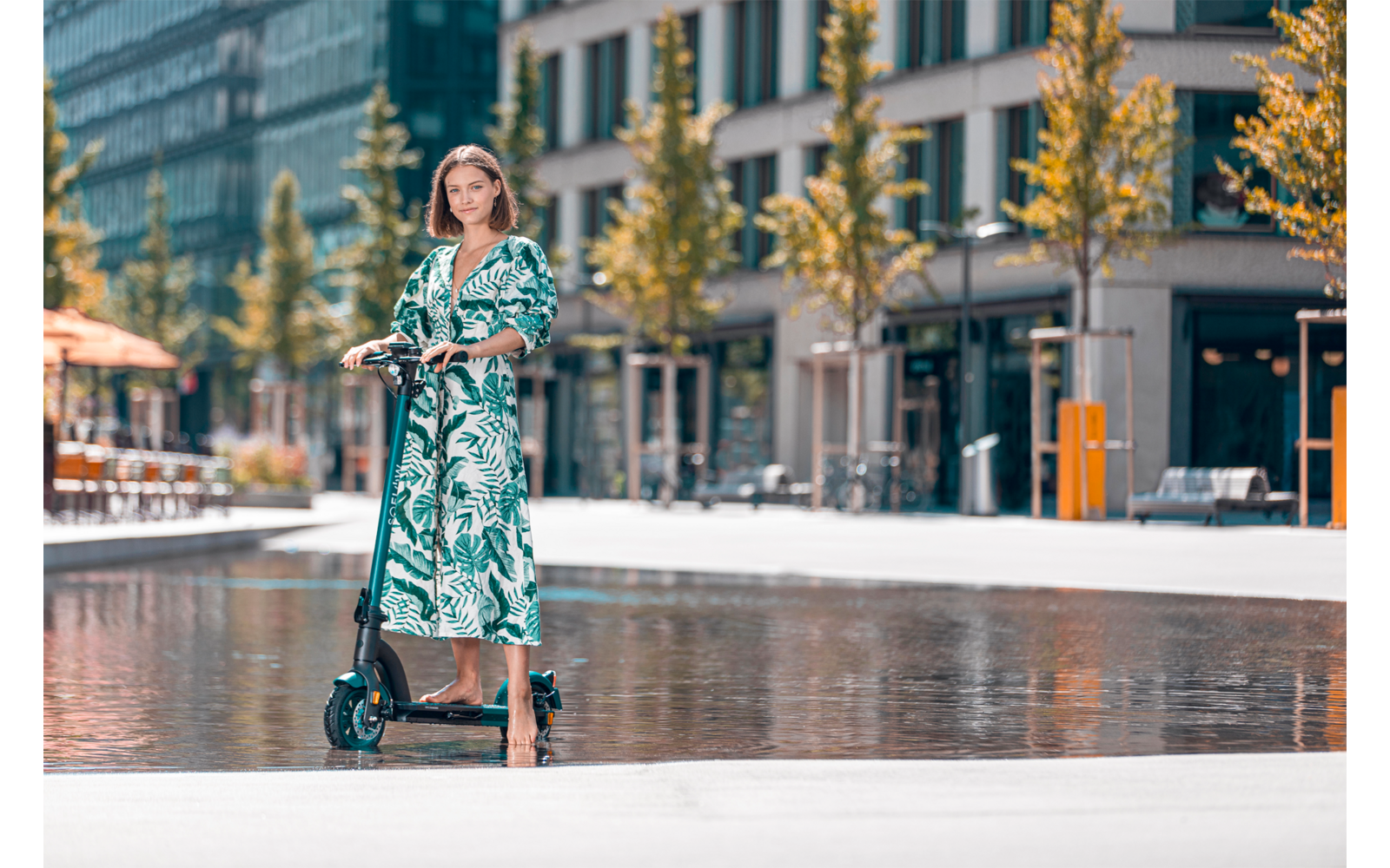 Donna in vestito a motivi in piedi su un monopattino in una piazza della città