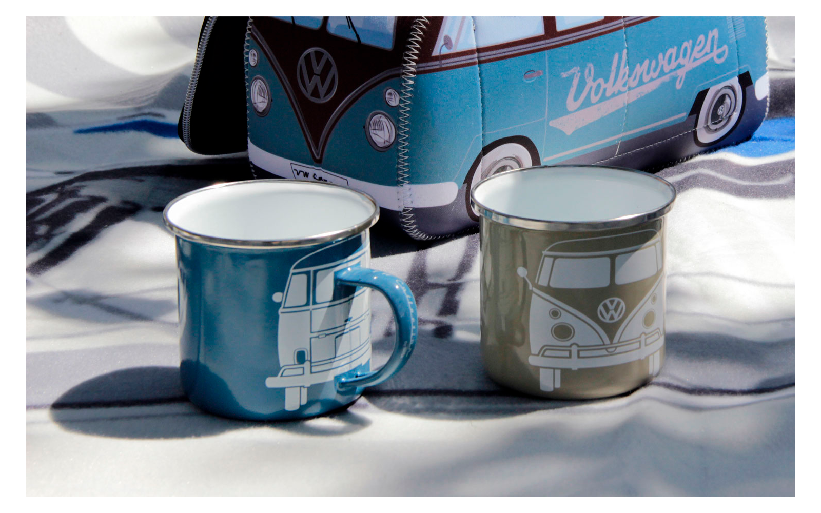 Two enamel mugs in blue and gray in front of a model Volkswagen bus