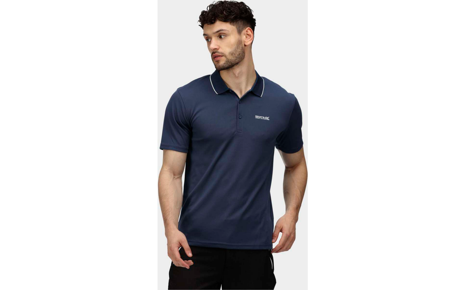 Mann mit kurzem dunklem Haar trägt ein dunkelblaues Poloshirt und schwarze Hosen, steht vor weißem Hintergrund