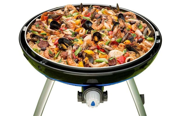 Paella mit Meeresfrüchten in einer schwarzen Paella-Pfanne auf einem Stativ mit Gasbrenner