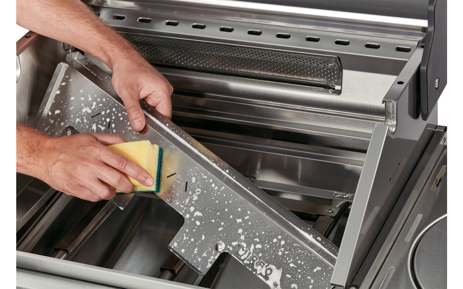 Hands cleaning a metal grill with a sponge