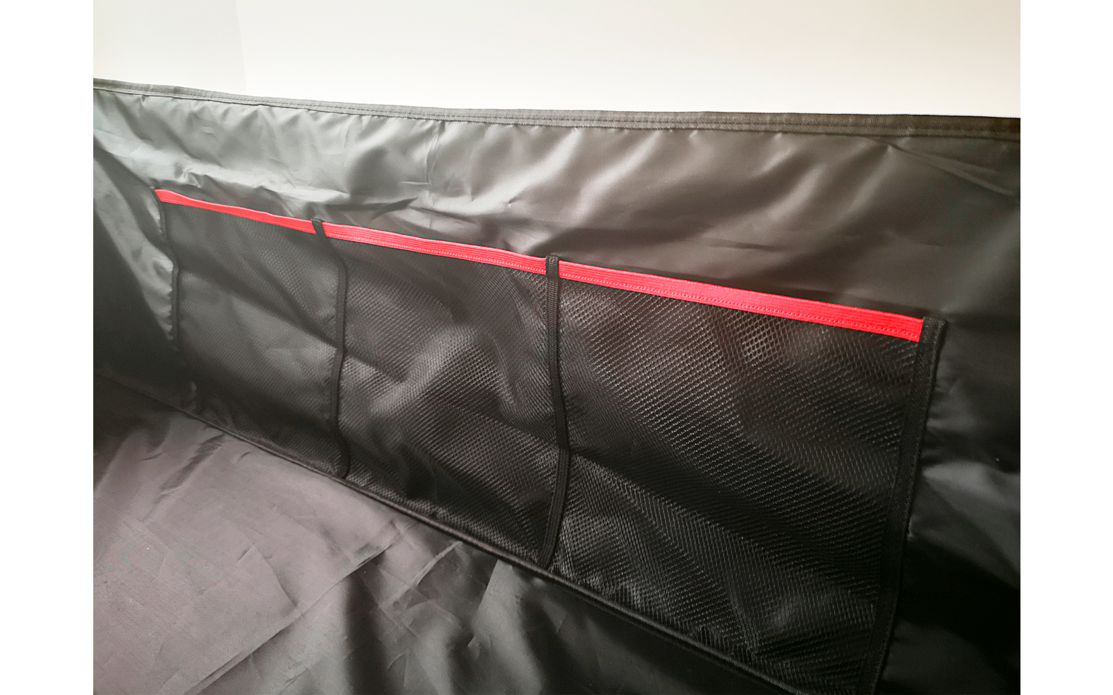 Schwarze Tasche mit drei Fächern und roten Reißverschlüssen an heller Wand