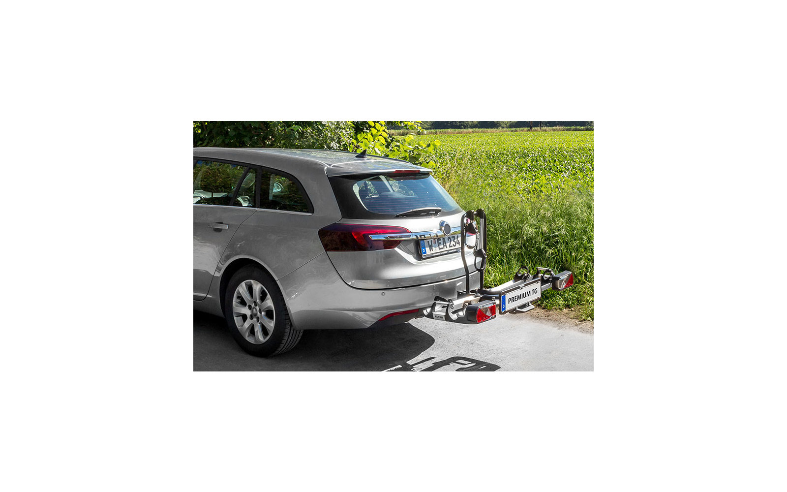 Silberner Kombi mit Fahrradträger auf der Anhängerkupplung, im Hintergrund eine grüne Wiese