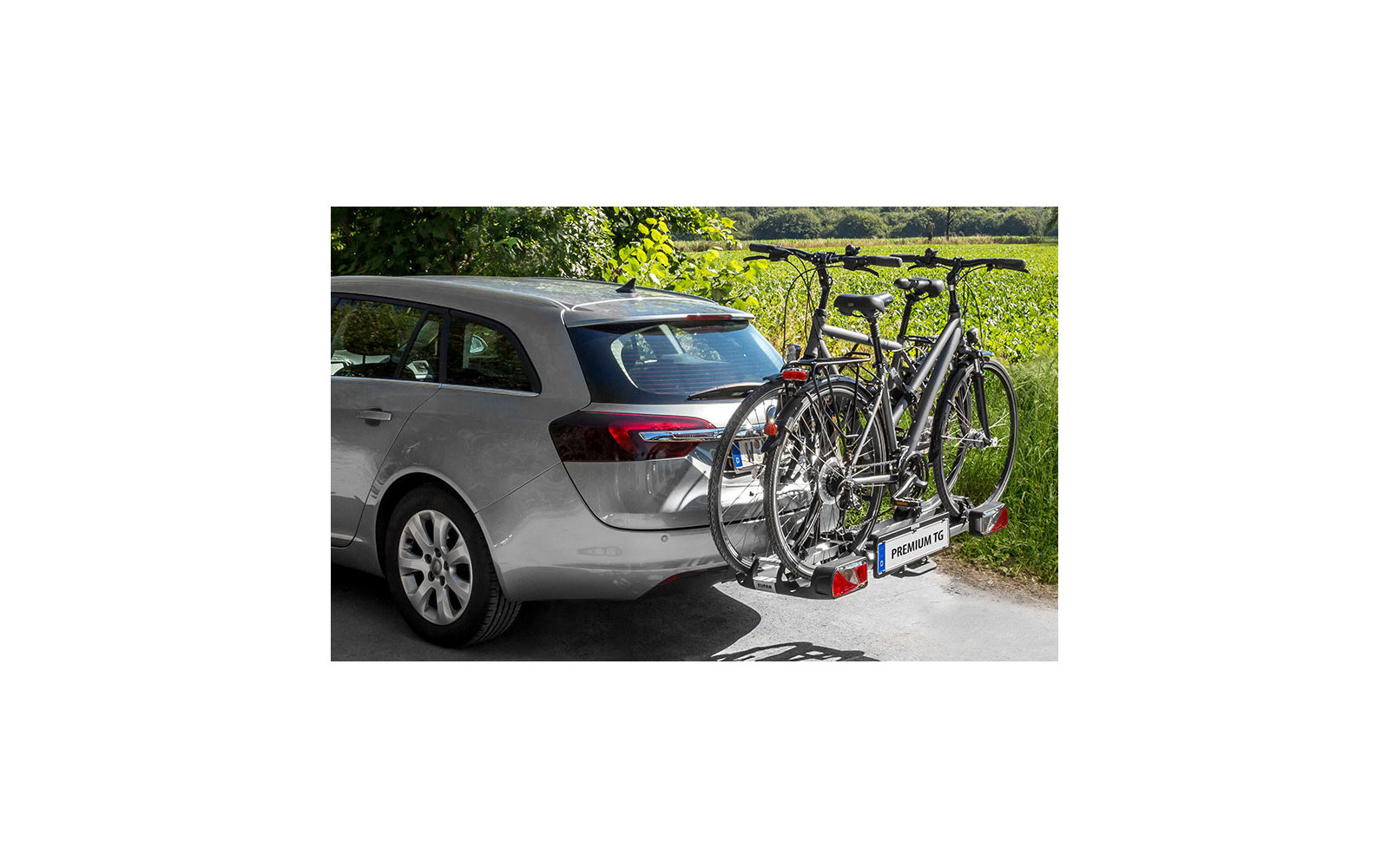 Silberner Wagen mit zwei Fahrrädern auf einem Heckträger, im Hintergrund ein Garten mit grünem Rasen