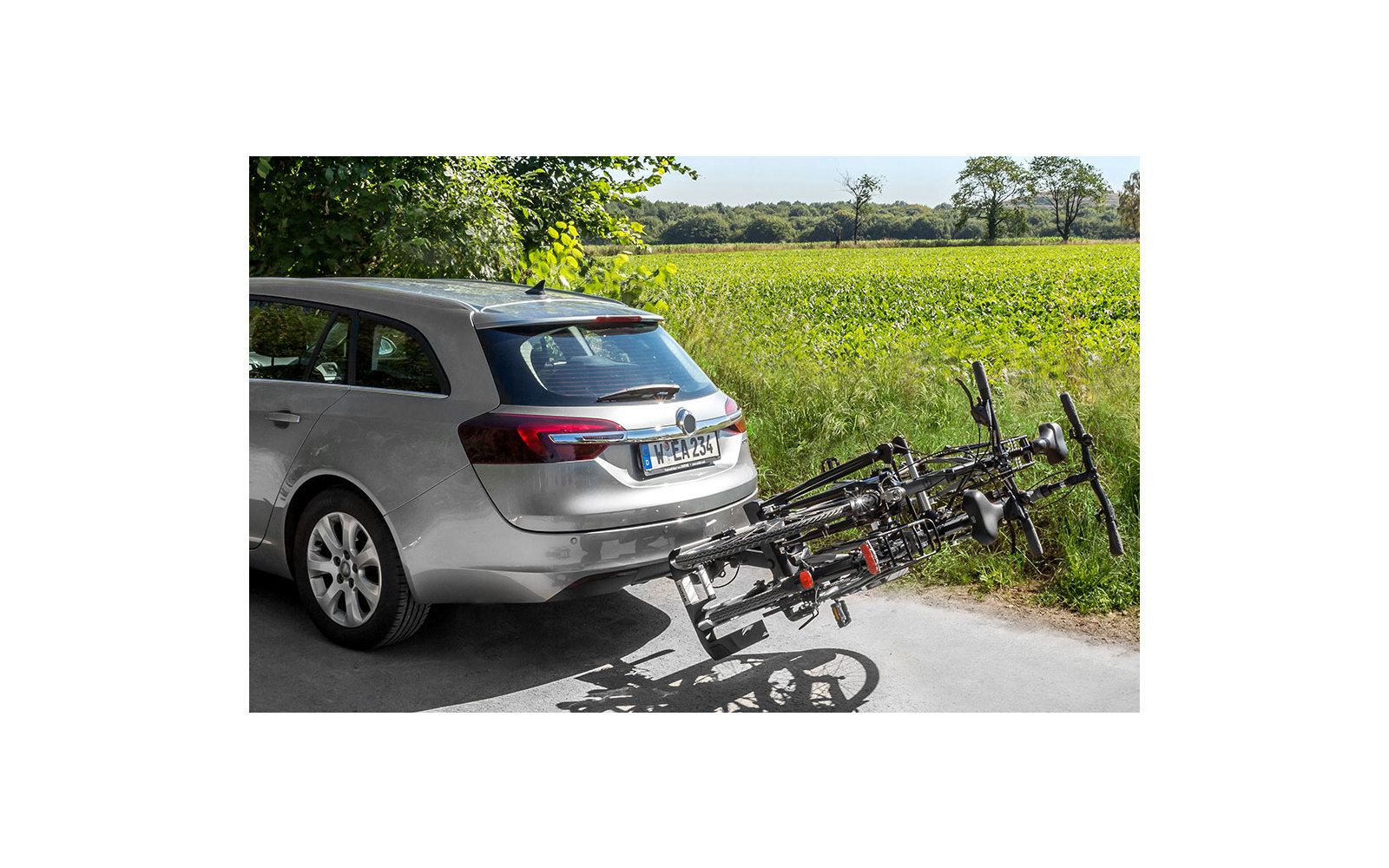 Silberner SUV mit Fahrradträger auf der Anhängerkupplung, zwei Fahrräder montiert, steht auf einem Weg mit grünem Feld im Hintergrund