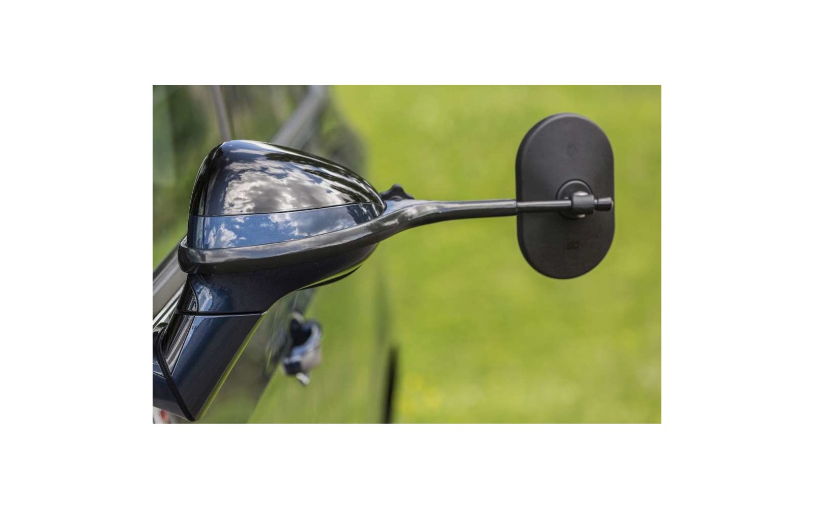 Nahaufnahme eines schwarzen Motorradspiegels und eines Teils des Lenkers vor unscharfem grünem Hintergrund