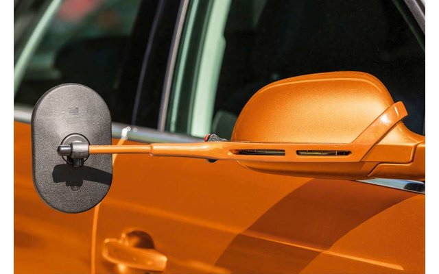 Ein weißer Kaffeebecher auf einem Holztisch, im Hintergrund unscharf ein geöffnetes Buch und eine Pflanze