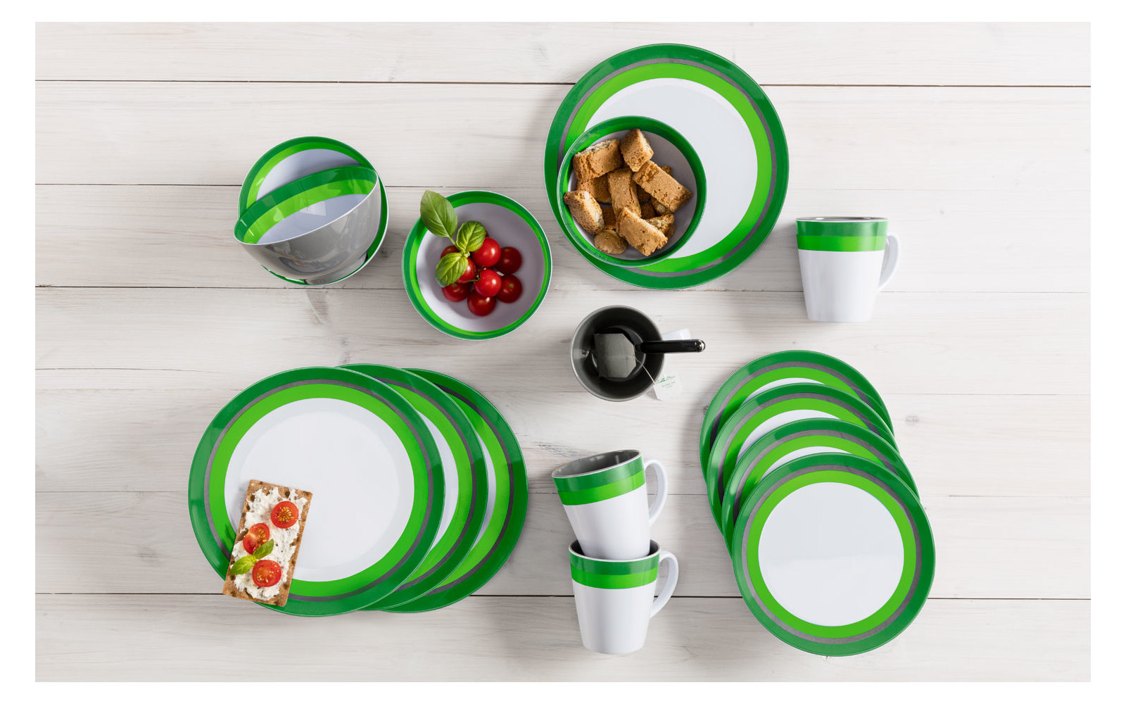 Mehrere grüne und weiße Camping-Geschirrteile auf einem weißen Holztisch