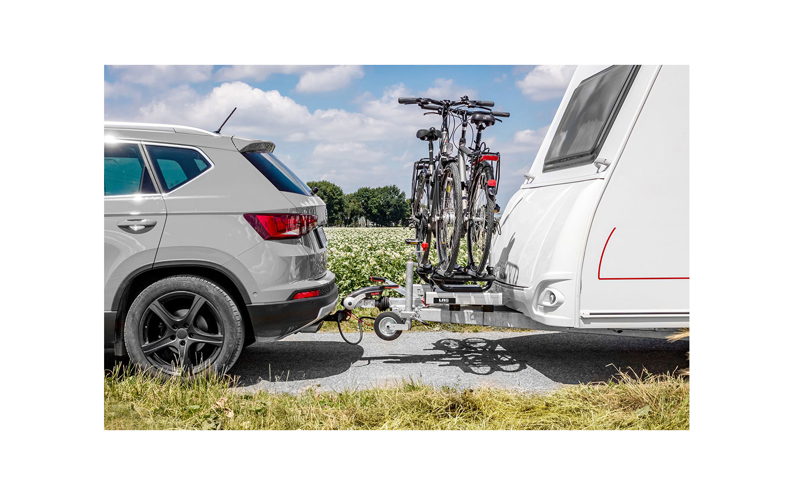 Auto zieht einen Wohnwagen mit zwei Fahrrädern auf einem Fahrradträger