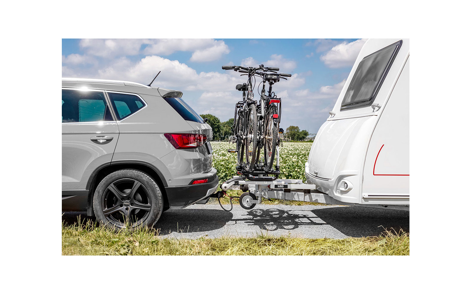 Ein weißes Auto zieht einen Wohnwagen, an der Anhängerkupplung sind zwei Fahrräder befestigt
