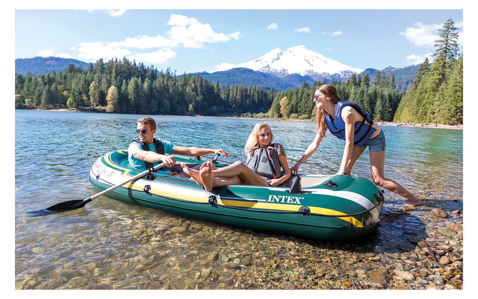 Drei Personen in einem Schlauchboot am Ufer eines Sees mit Bergen im Hintergrund