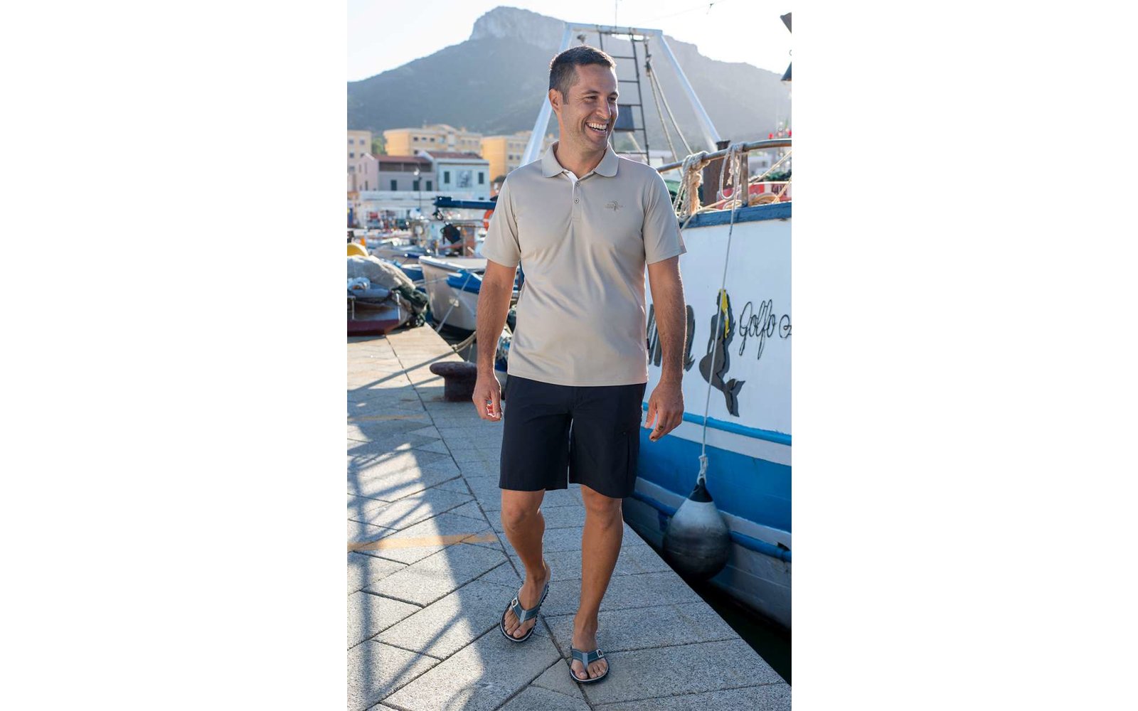 Mann in weißem T-Shirt und dunkler Shorts steht auf einem Steg neben einem Boot