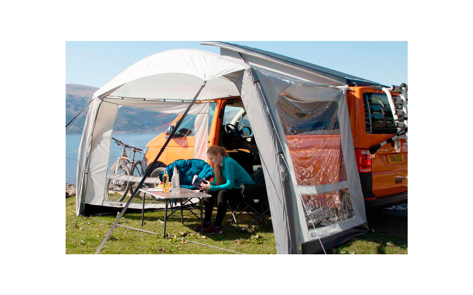 Person sitting at a table under a white canopy next to an orange camper