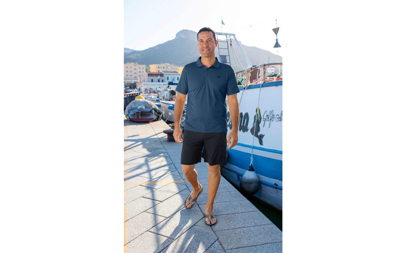 Mann in blauem Poloshirt und schwarzen Shorts geht am Hafen entlang