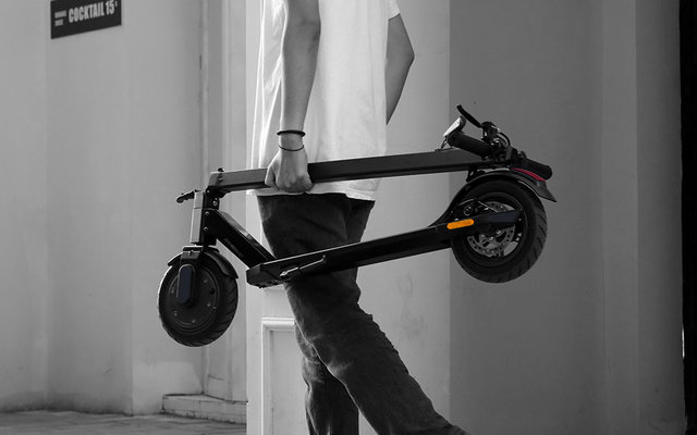 Elektrischer Scooter steht an einem Metallgeländer befestigt vor einer weißen Wand